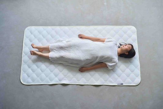 上位版ベッドパッドの上で、あお向けに寝る女性を真上から写した写真（SLEEP HEXAGON）