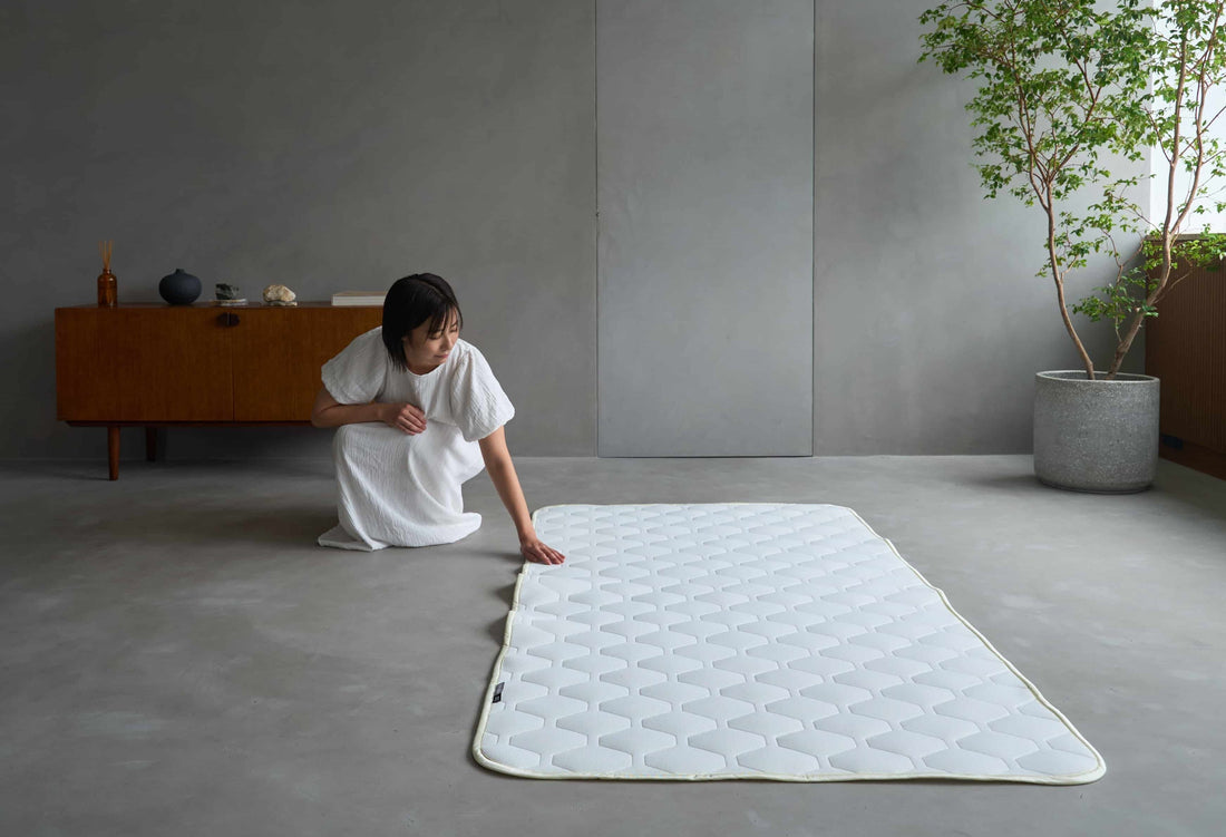 床に上位版ベッドパッドを広げる女性（SLEEP HEXAGON）